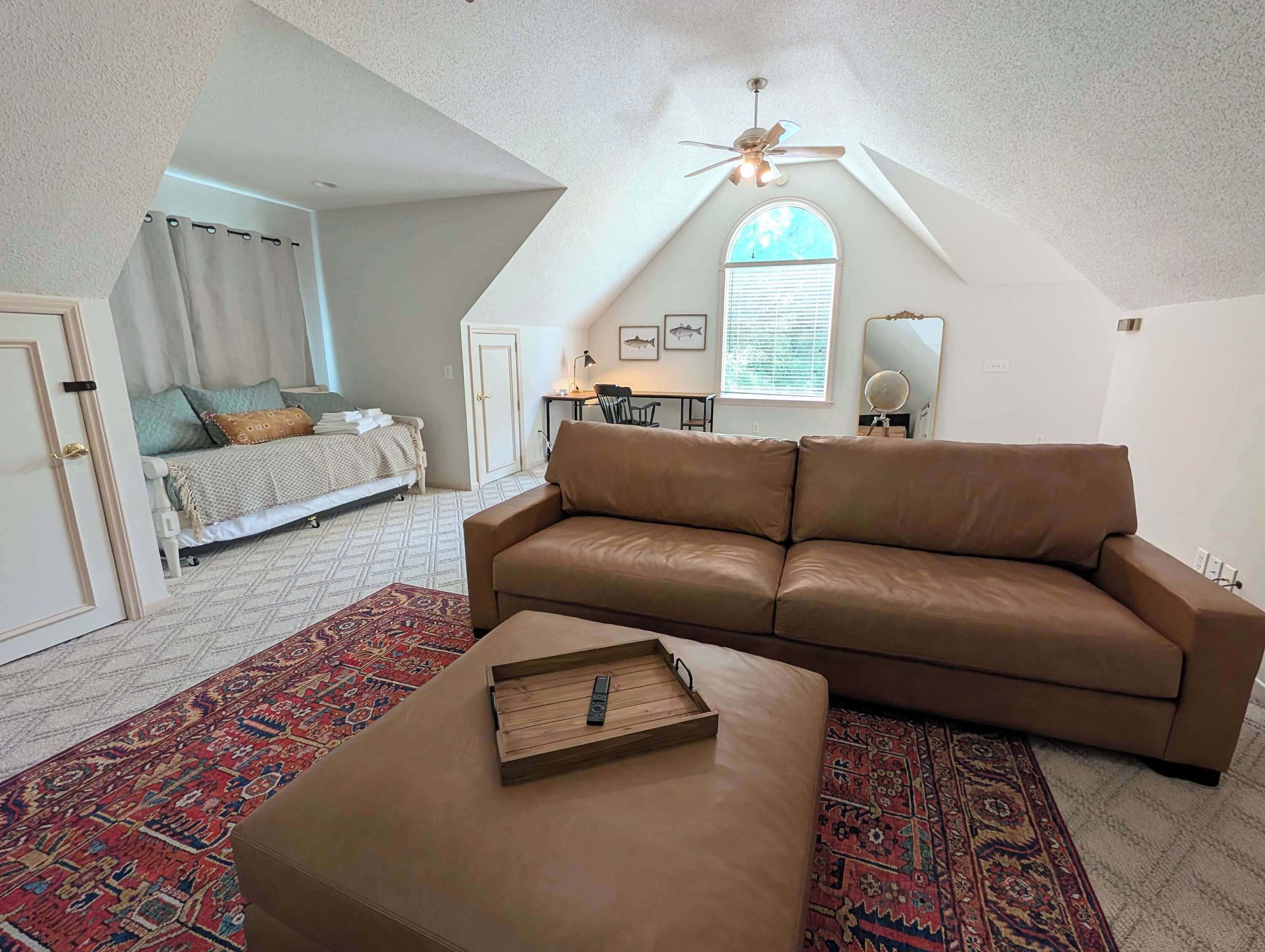 Un dormitorio estilo loft con techo inclinado, un sofá de cuero marrón, un tapete estampado y una bandeja de madera sobre un reposapiés.