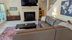 A living room with a fireplace, a sofa, a coffee table, a TV, and a world map on the wall. - Lake Days Getaway - Lakeside Family Escape Near Hillsborough (Hillsborough)