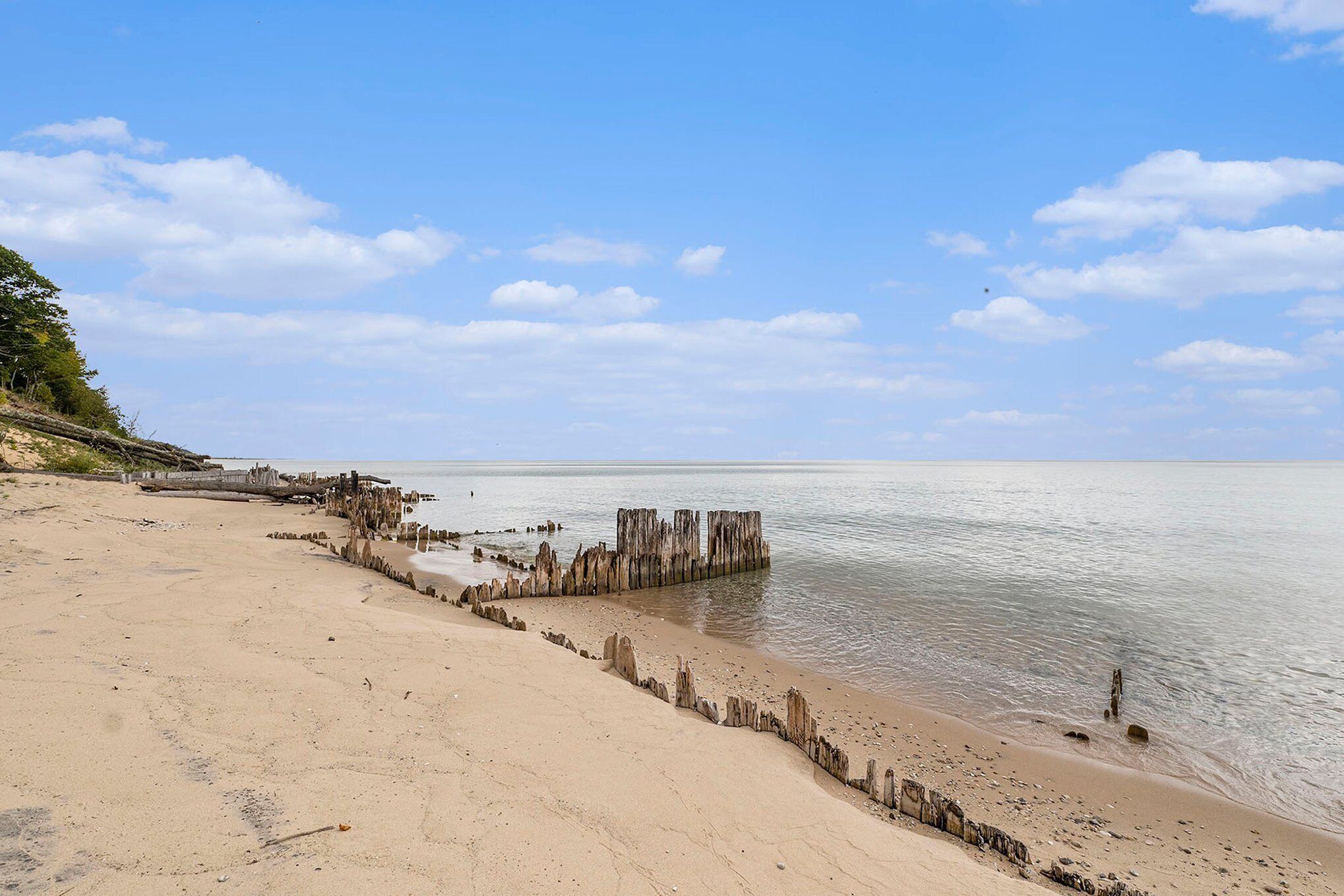 A beach with a wooden structure extending into the water, a clear sky, and calm sea.