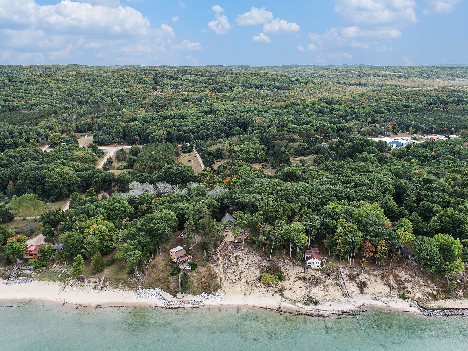 An aerial view of a coastal area with dense greenery, a sandy beach, and scattered buildings.
