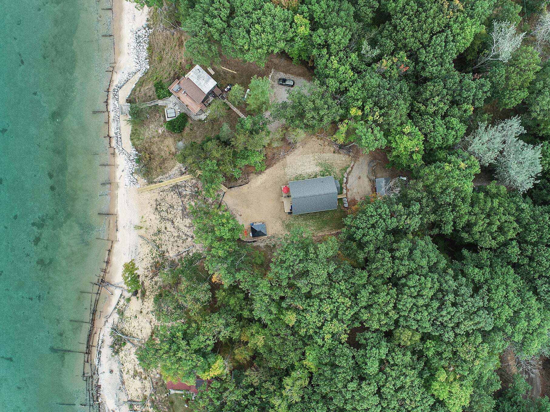 An aerial view of a coastal property with a beach, a house, and dense forest.