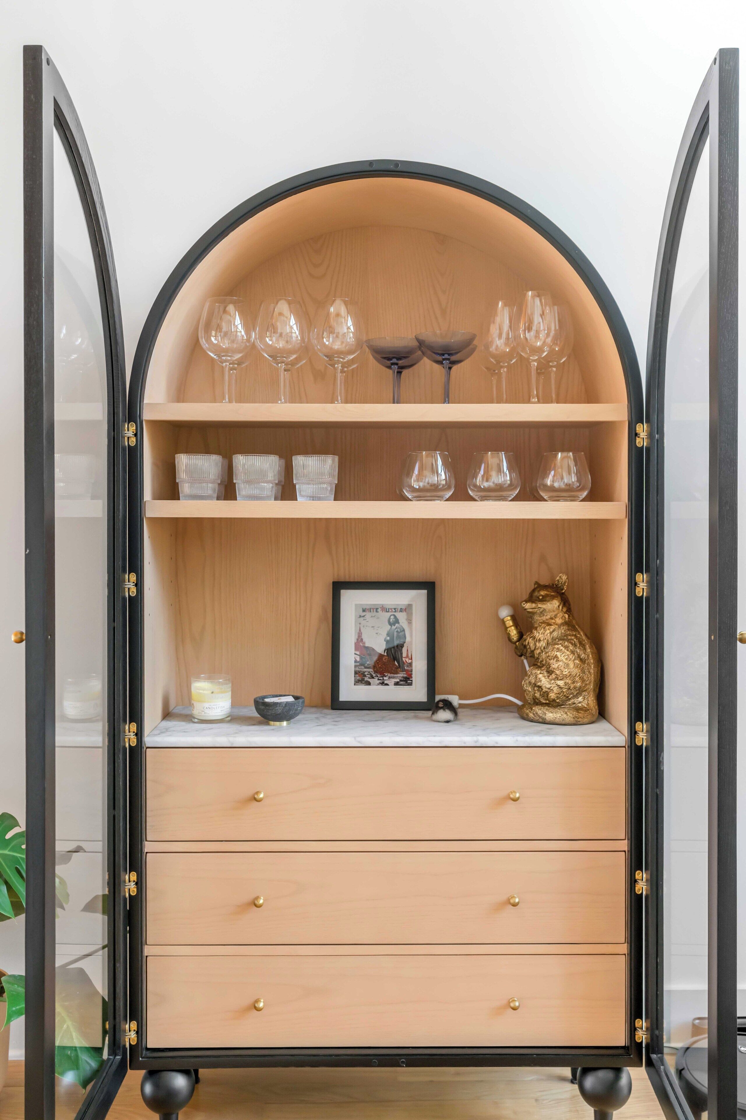 A wooden cabinet with glassware and a framed picture.