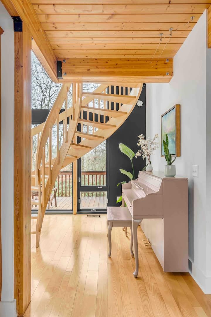 A modern interior with a wooden staircase, a piano, and a view of the outdoors.
