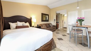 Una camera d'albergo con un letto, un divano, un tavolo da pranzo con sedie, uno specchio e una sveglia appesa al muro.
