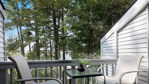 Un balcone con due sedie e un tavolino, immerso nel verde alberato e affacciato su una casa.