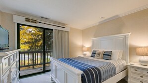 A bedroom with a large bed, a dresser, a nightstand, and a view of a balcony with a door. - Gorgeous Grand Traverse Bay Beach Front The Shores - 5704 (Williamsburg)