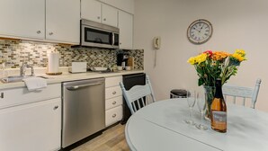 A modern kitchen with white cabinets, a microwave, a coffee maker, and a dining table with a vase of flowers and wine glasses. - Gorgeous Grand Traverse Bay Beach Front The Shores - 5704 (Williamsburg)