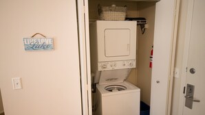 A laundry room with a washing machine and dryer, a basket on the dryer, and a sign on the wall. - Gorgeous Grand Traverse Bay Beach Front The Shores - 5704 (Williamsburg)