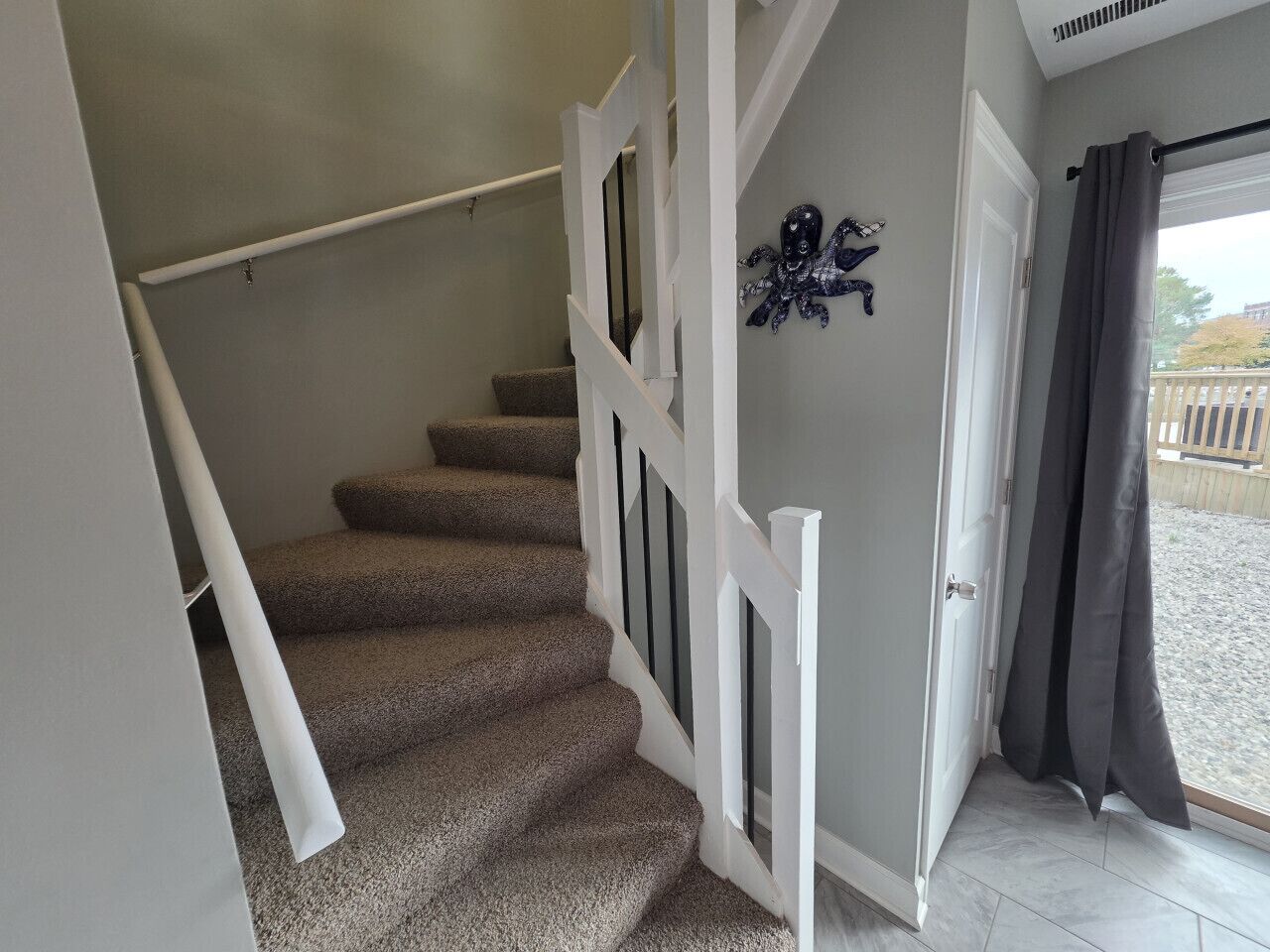 A staircase with carpeted steps and white railings, leading to a door with a dark curtain.