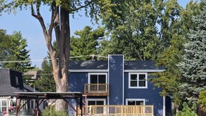 A two-story house with a dock extending into a calm body of water, surrounded by lush greenery and trees. - The Riverwalk Retreat on the Fox - Waterfront Vacation Rental in Downtown Mchenry 3br/2ba Home With Private Pier (McHenry)