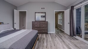 A bedroom with a bed, a dresser, and a sliding glass door leading to a balcony. - The Riverwalk Retreat on the Fox - Waterfront Vacation Rental in Downtown Mchenry 3br/2ba Home With Private Pier (McHenry)
