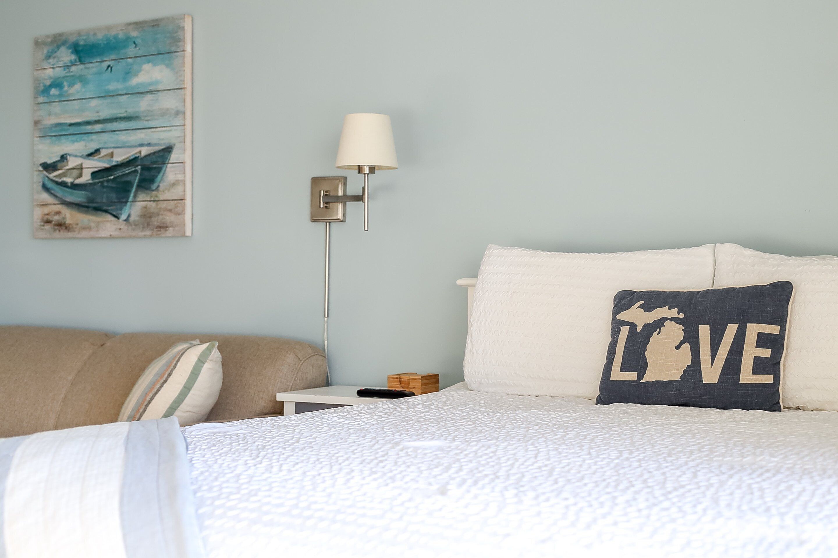 Un dormitorio con una cama, almohadas, una mesita de noche, una lámpara y un cuadro en la pared.