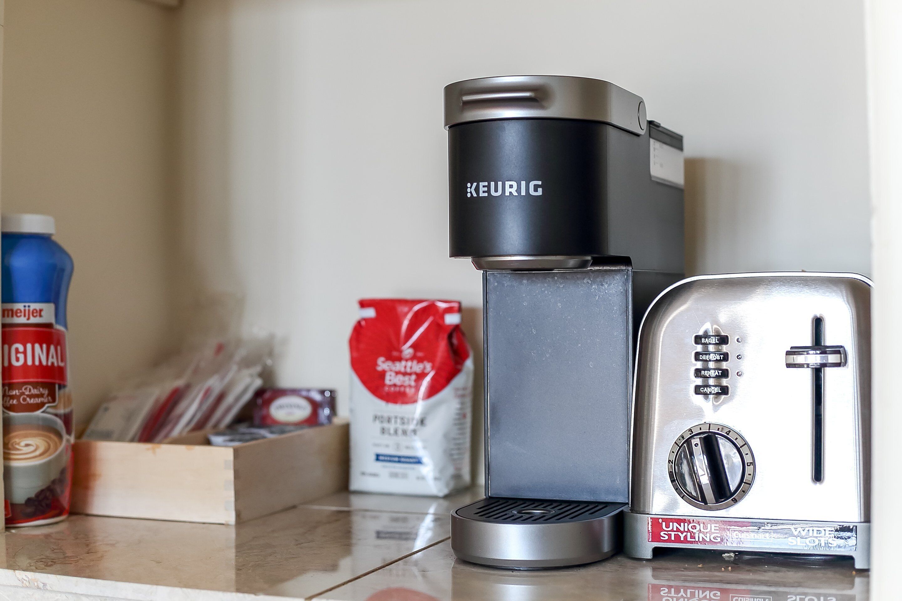 A coffee maker, a toaster, a coffee jar, and a bag of coffee pods on a kitchen counter.