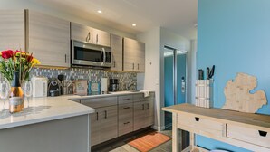 Een moderne keuken met een magnetron, toaster en koffiezetapparaat. Er is een houten kookeiland met een bloevas en een fles wijn. De keuken heeft een blauwe accentmuur en een houten wereldkaart decoratie.