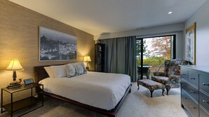 Een hotelkamer met een groot bed, twee bedlampen, een stoel, een dressoir en een stadsgezicht door een groot raam.