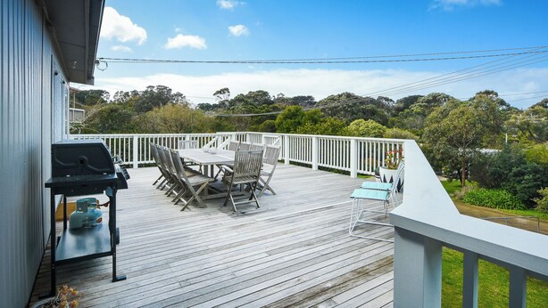 A wooden deck with a white railing, a table with chairs, and a barbecue grill. - Coastal Haven, 5 minute walk to beach. (Flinders)