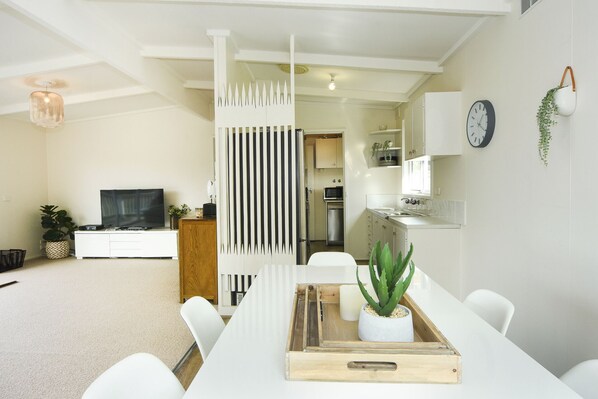A modern living room with a TV, white furniture, a wooden divider, and a dining area with a tray.