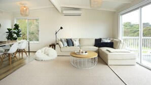 A modern living room with a sofa, coffee table, and a dining area with chairs. - Coastal Haven, 5 minute walk to beach. (Flinders)