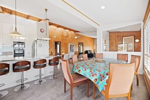 A modern kitchen with wooden accents, a dining area with a colorful tablecloth, and a bar with stools. - Cabana-Rama: The Ultimate Family Retreat (Tuross Head)