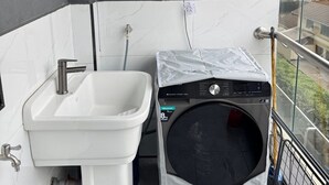 A compact bathroom with a white sink, a small washing machine, and a grey cabinet above. - 1 bedroom kilimani centrally located (Nairobi)