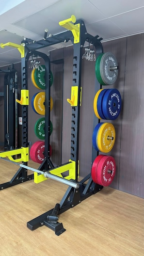A weightlifting station with a squat rack, barbell, and weight plates. - Cozy 1BR in Kilimani - Epic Balcony & City Views (Nairobi)