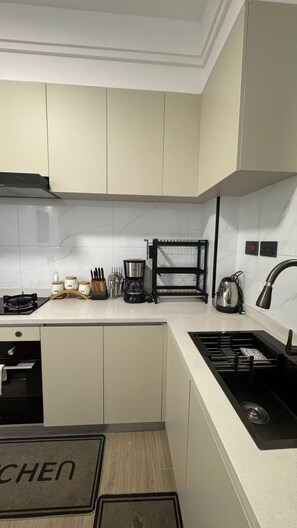 A modern kitchen with white cabinets, a black coffee maker, and a sink. - Cozy 1BR in Kilimani - Epic Balcony & City Views (Nairobi)
