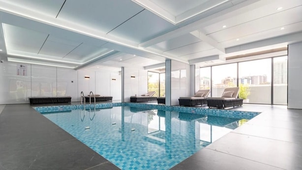 A modern indoor swimming pool with clear glass walls, black lounge chairs, and a tiled floor. - 1 bedroom kilimani centrally located (Nairobi)