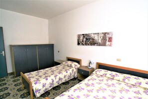 Ein Zimmer mit zwei Einzelbetten, einem Kleiderschrank, einem Nachttisch und einem Wandbild.