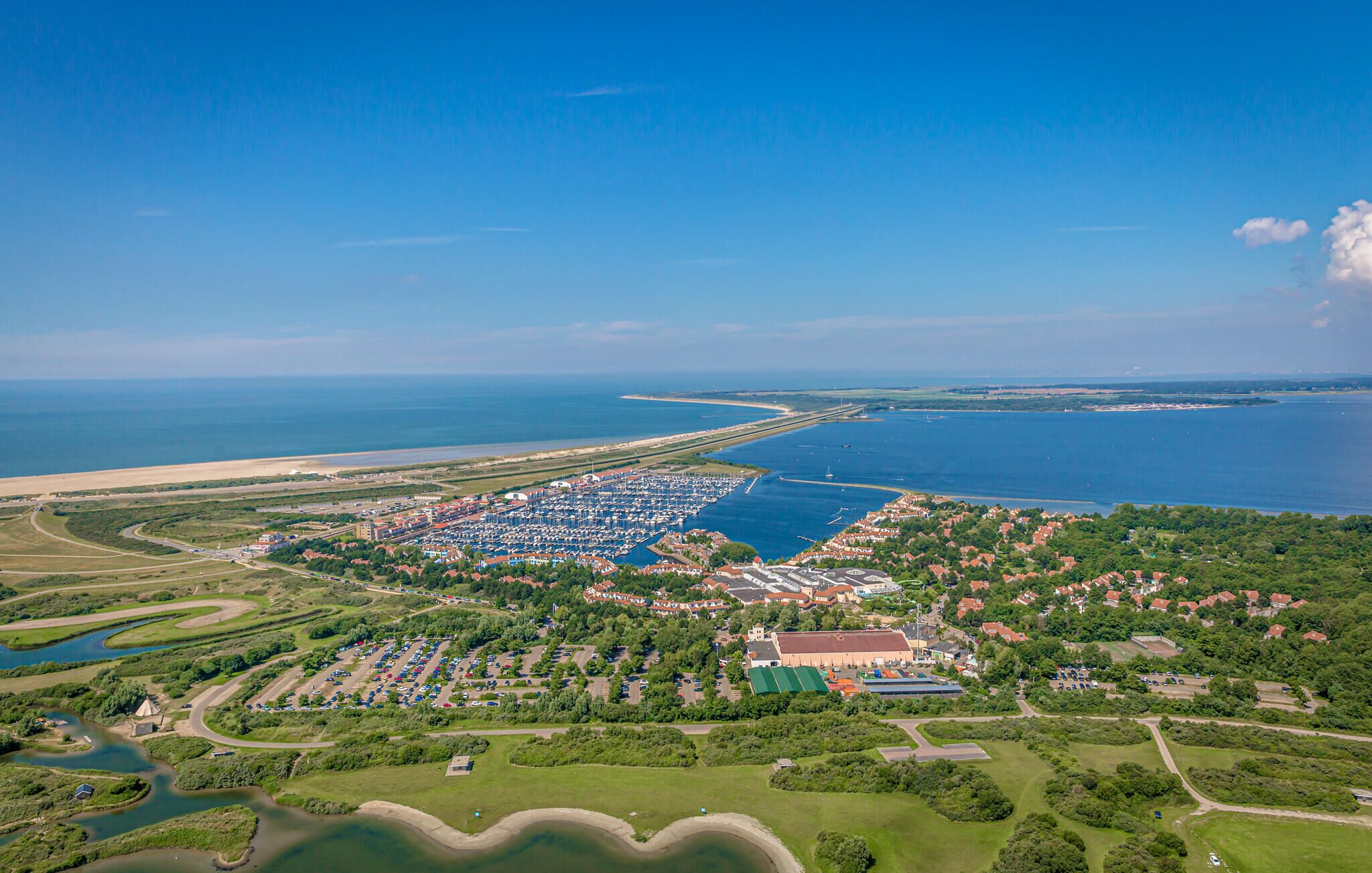 Vista aérea de un pueblo costero con un puerto deportivo, zonas verdes y áreas residenciales.
