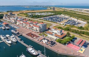 A marina with boats docked, a parking area, and buildings with red roofs.