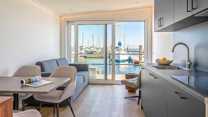 Una sala de estar moderna con comedor, cocina y puerta corrediza de vidrio que da a vista de un puerto deportivo.