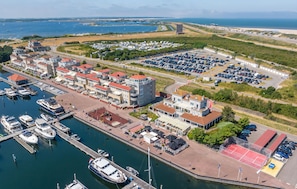A marina with boats docked, a parking area, and buildings with red roofs.