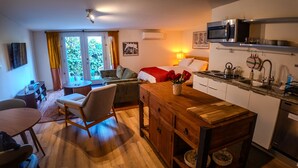 Habitación compacta y bien iluminada con kitchenette, comedor y cama.