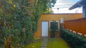 A pathway leading to a door, surrounded by lush greenery and a wooden fence.