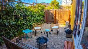 A patio with four wicker chairs, a small blue table, a fire pit, and a wooden bench.