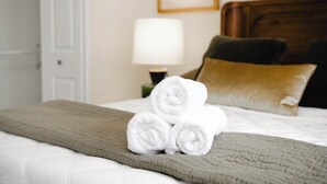 A neatly made bed with rolled white towels, a brown quilt, and a wooden headboard. - Two Sparrows - Birmingham Townhome with King Suite (Birmingham)