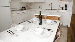 A modern kitchen with white cabinetry, a marble countertop, and a dining table set for four. - Two Sparrows - Birmingham Townhome with King Suite (Birmingham)