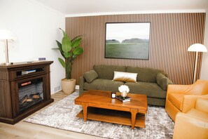 Een woonkamer met een open haard, een bank, een bijzettafeltje en een groot raam met uitzicht op een veld.