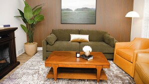 A living room with a sofa, a coffee table, a lamp, and a large painting on the wall. - Two Sparrows - Birmingham Townhome with King Suite (Birmingham)