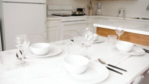 A white marble kitchen with white cabinets, a stove, and a dining table set with white bowls, glasses, and cutlery. - Two Sparrows - Birmingham Townhome with King Suite (Birmingham)