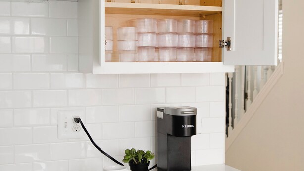 A kitchen with white cabinetry, a coffee maker, a potted plant, and a countertop with a cutting board and a mug. - Two Sparrows - Birmingham Townhome with King Suite (Birmingham)