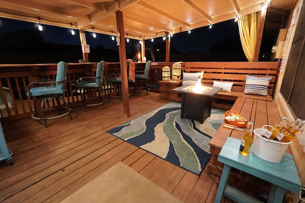 Una terraza al aire libre con mobiliario de madera, una mesa con botellas y un banco.