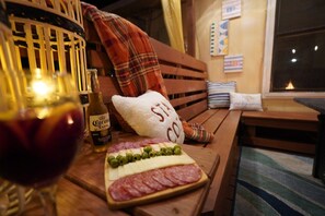 Un banc en bois, une bouteille de bière Corona, un verre de vin rouge et une planche de charcuterie garnie de fromage, d’olives et de saucisson.
