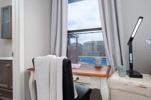 Ett rum med ett skrivbord, en stol, ett fönster med gardiner, en lampa och en mugg på skrivbordet.