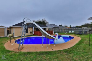 Un jardin avec une piscine, un toboggan et un flotteur en forme de cygne.