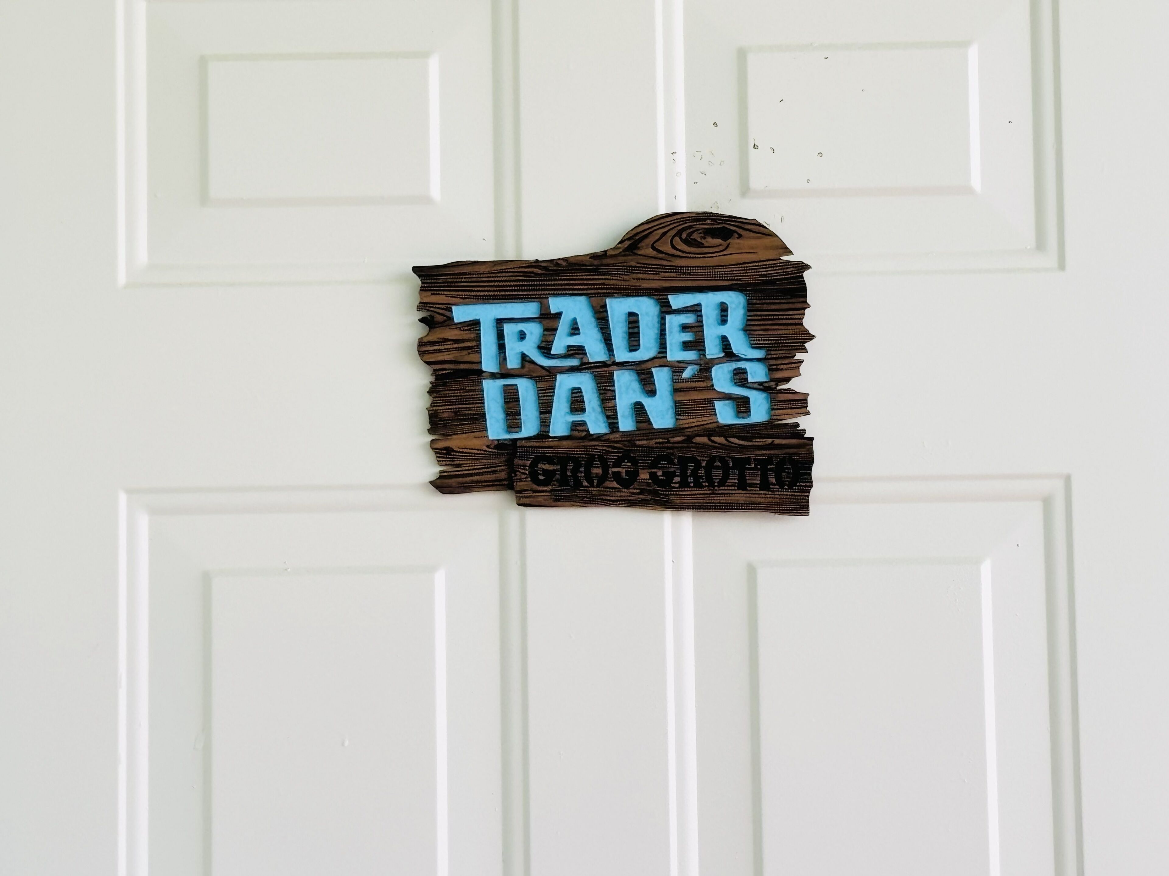 Una puerta blanca con un letrero de madera que dice "TRADER DAN'S" en letras azules.
