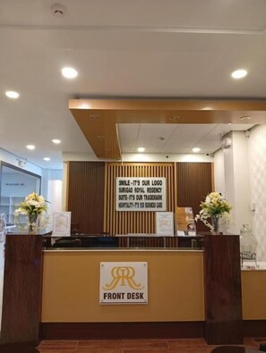 A reception desk with a sign reading "SMILE-IT'S OUR LOGO SURIGAO ROYAL REGENCY SUITE-IT'S OUR TRADEMARK HOSPITALITY-IT'S OUR BUSINESS CARD". - Surigao Royal Regency Suites (Surigao)