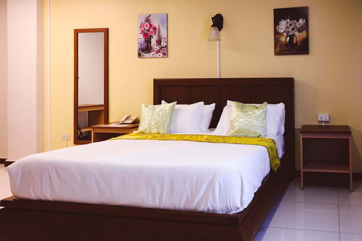 A neatly made bed with white linens and a yellow throw blanket, a bedside table with a lamp, and two wall-mounted paintings.