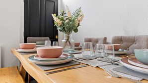 Una mesa de comedor bien dispuesta con platos rosa y azul, copas de cristal transparentes y un jarrón con flores.