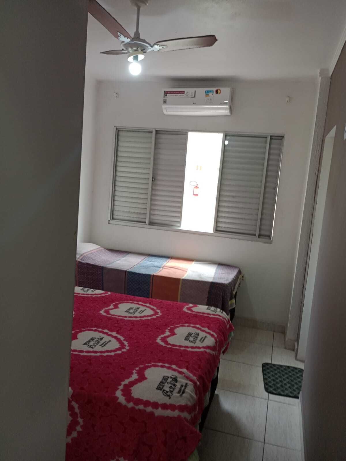 Une petite pièce étroite, avec un lit, un ventilateur de plafond et une fenêtre munie de stores.